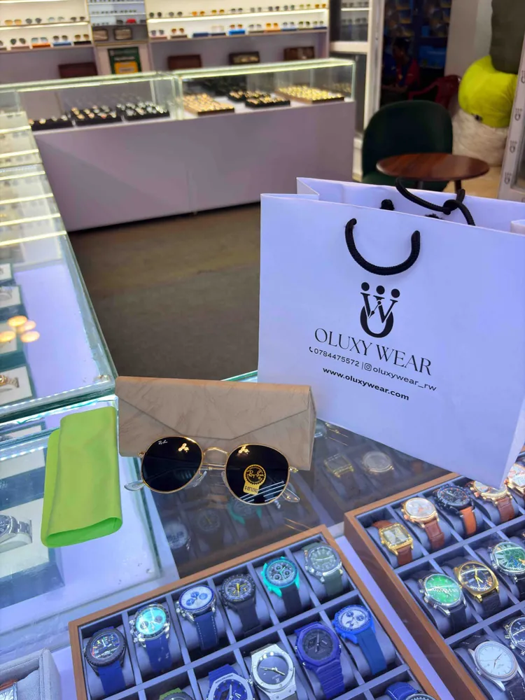 Round gold-framed sunglasses in front of their folding case, a green cleaning cloth and a white Oluxy Wear paper bag, on the shop counter