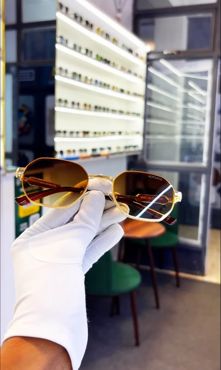 A pair of gold-framed sunglasses held up in a white-gloved hand inside the shop